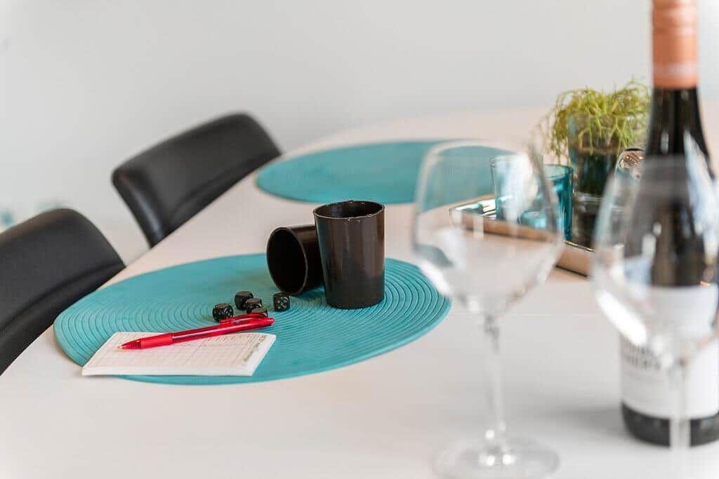 Tisch mit Platzdeckchen, Gläsern, Tasse, Würfeln und Stift