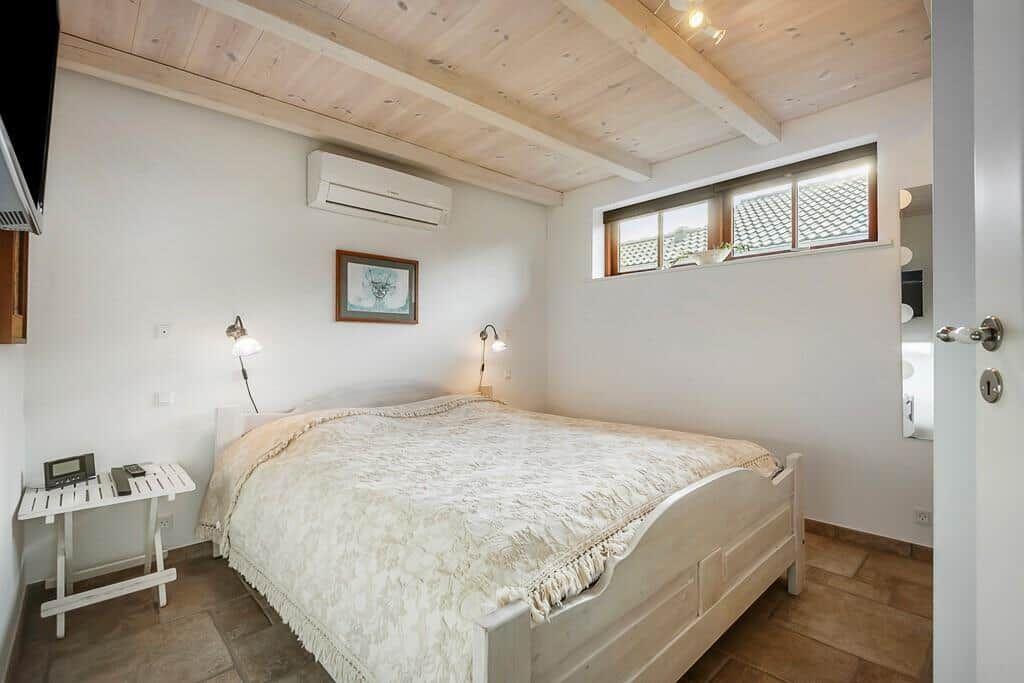 Schlafzimmer mit Bett, Nachttisch und Fenster. Holzdecke und Klimaanlage.