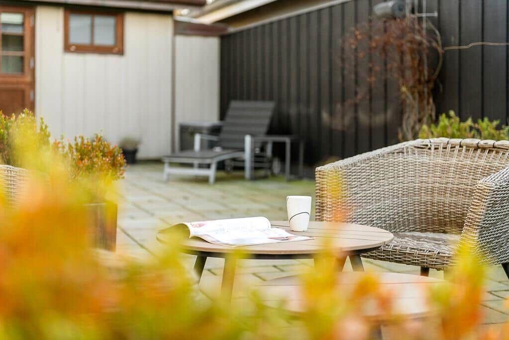 Außenbereich mit Tisch, Stühlen und Pflanzen. Im Hintergrund liegt eine Liege.