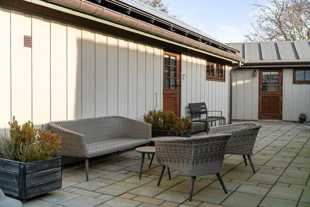 Außenbereich mit Rattanmöbeln und Pflanzen vor einem Holzhaus.