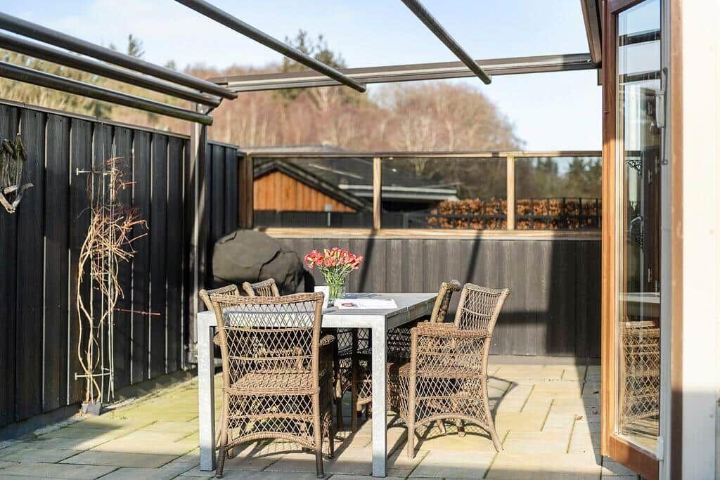 Terrasse mit Tisch, Stühlen und Blumen. Hintergrund: Holzzaun und Wald.