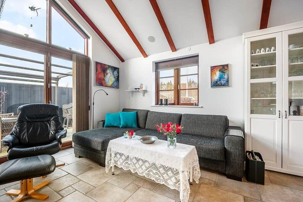 Wohnzimmer mit Sofa, Couchtisch und Sitzgelegenheit. Holzbalken und Fenster sichtbar.
