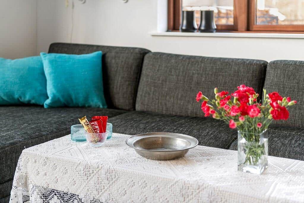Grauer Sofa mit türkisen Kissen, Tisch mit Blumen und Schale.