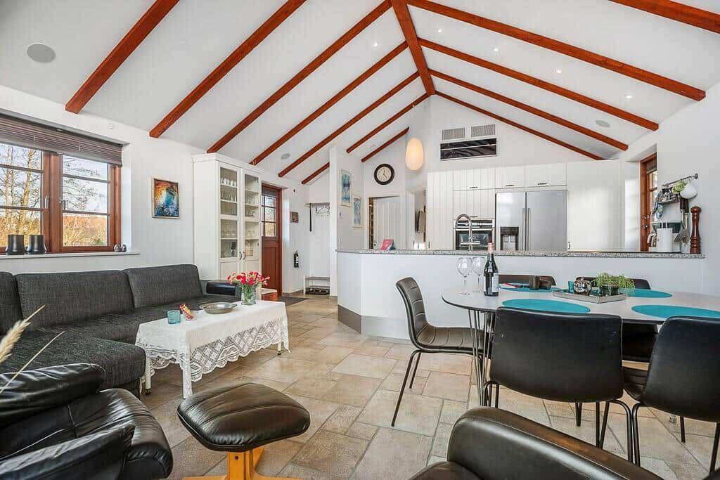 Wohn- und Essbereich mit Esszimmertisch, Sofa und Küchenzeile unter Holzdecke.
