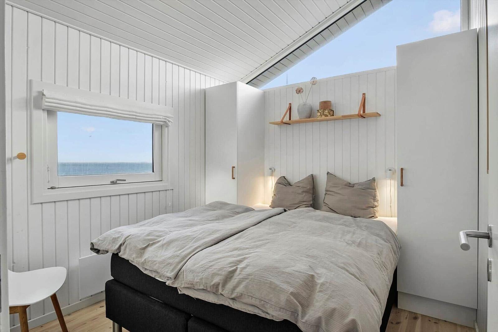 Bedroom with bed, window, and skylight. Wooden floor and white walls.