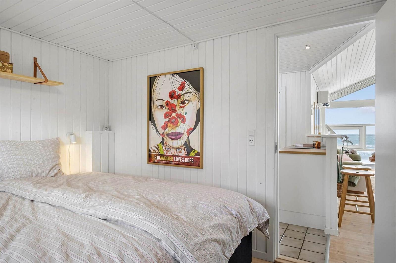 Bedroom with bed and wall art. Passage to living area with sea view.