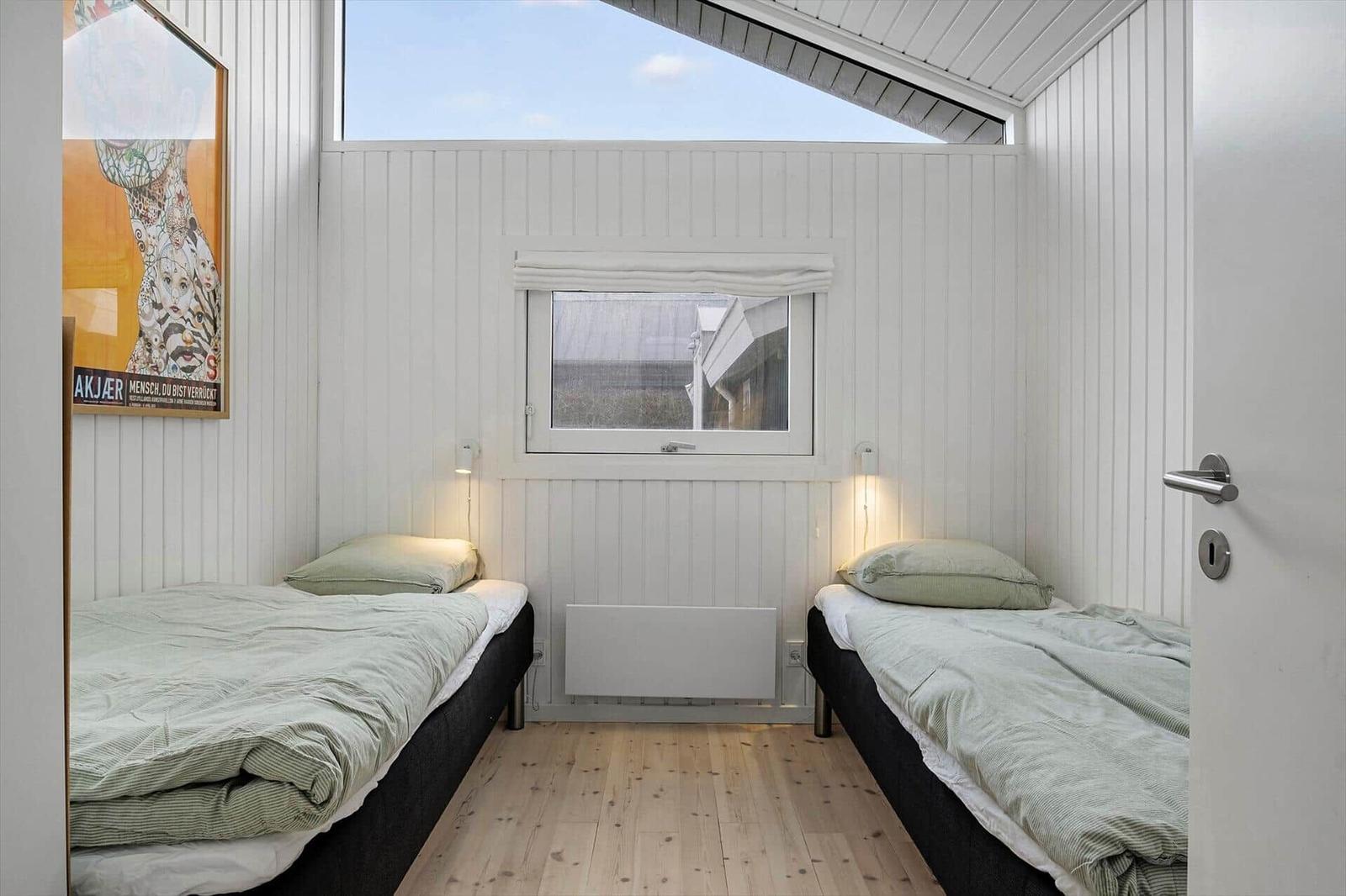 Two beds, window and wooden floor in a bedroom.