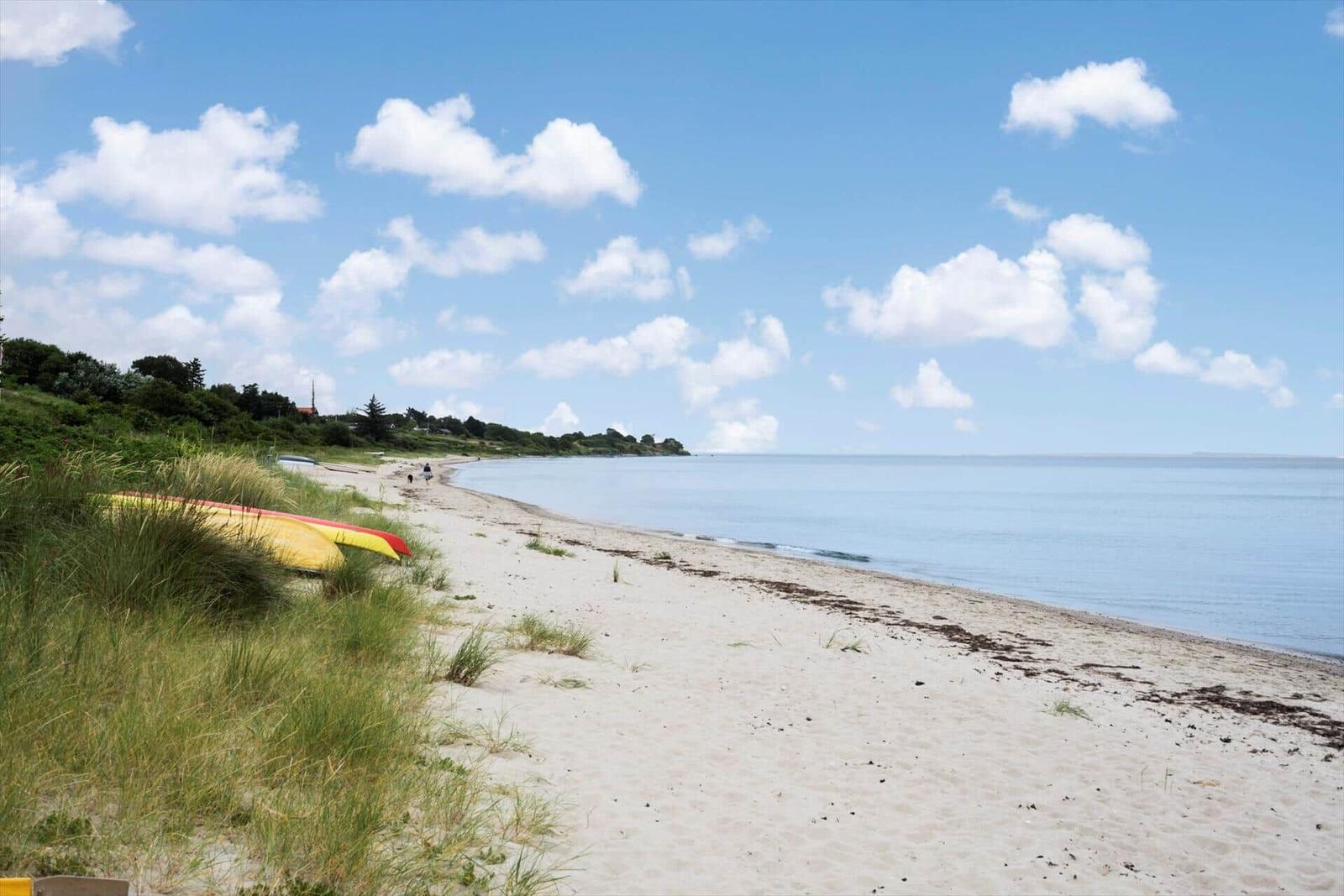 Beach with sand, grass, and a yellow kayak under a blue sky with white clouds.
