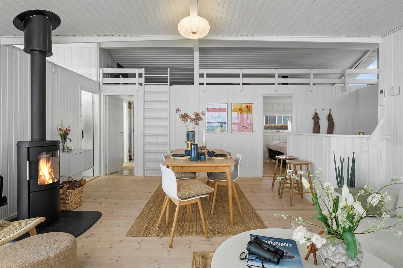 Living area with dining table, fireplace, and upper level. Modern furnishings with wooden floor.