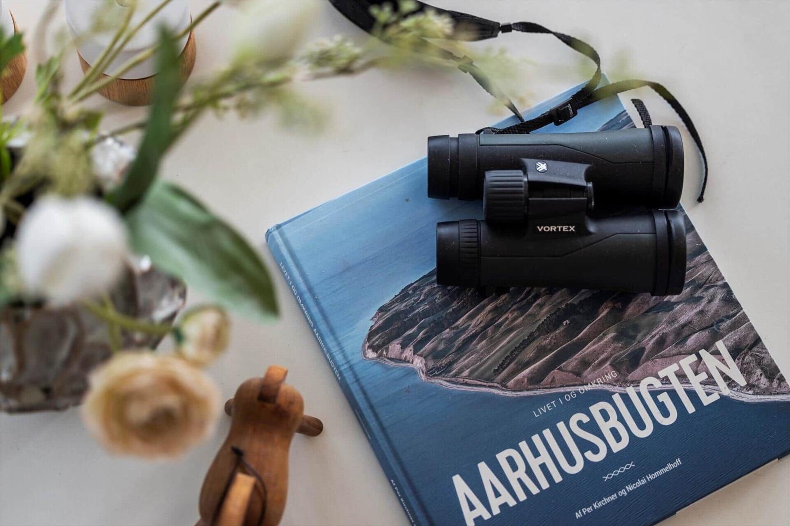 A book with binoculars on top and flowers beside it.