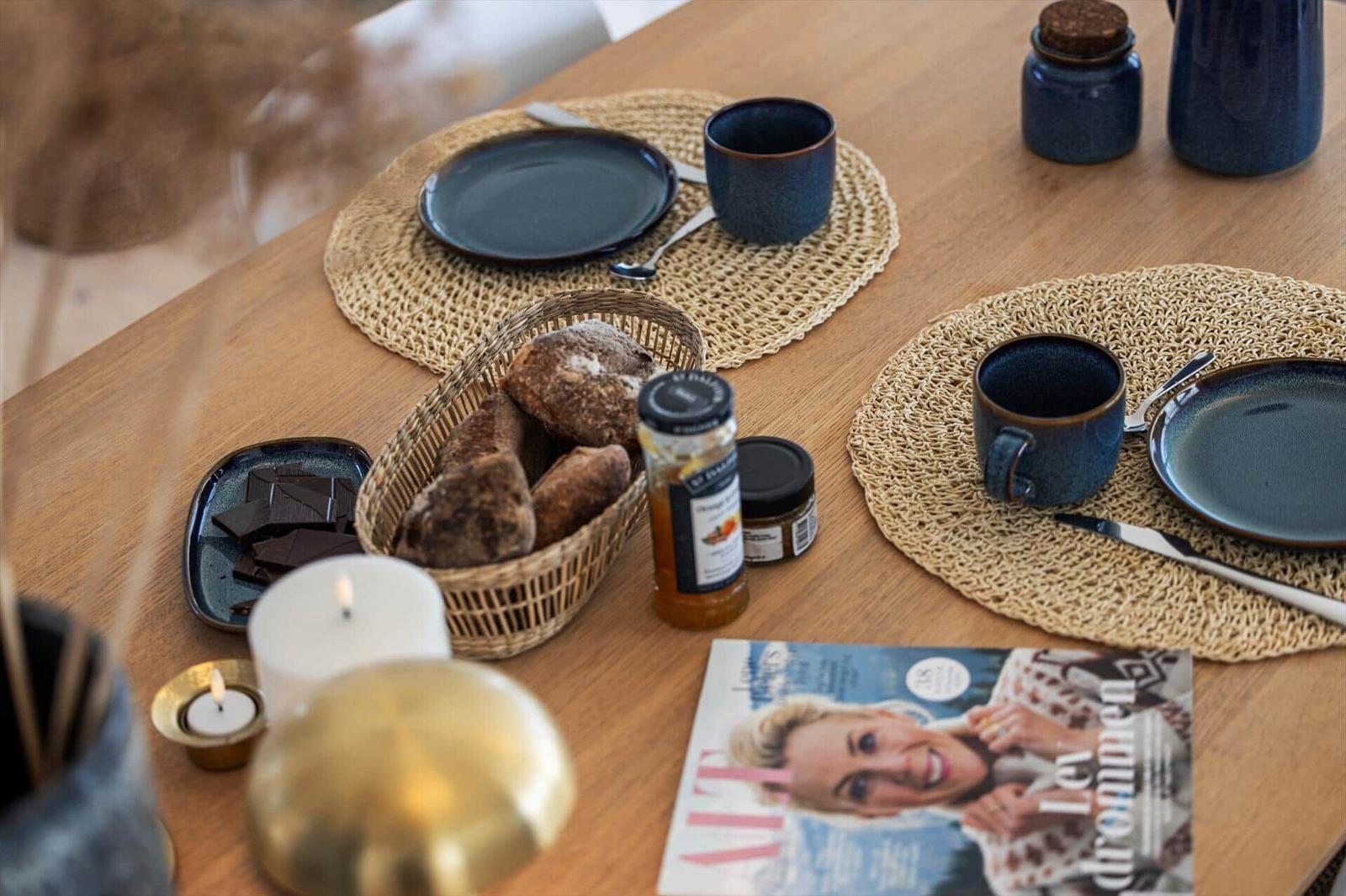 Wooden table with plates, mugs, bread, and magazine.