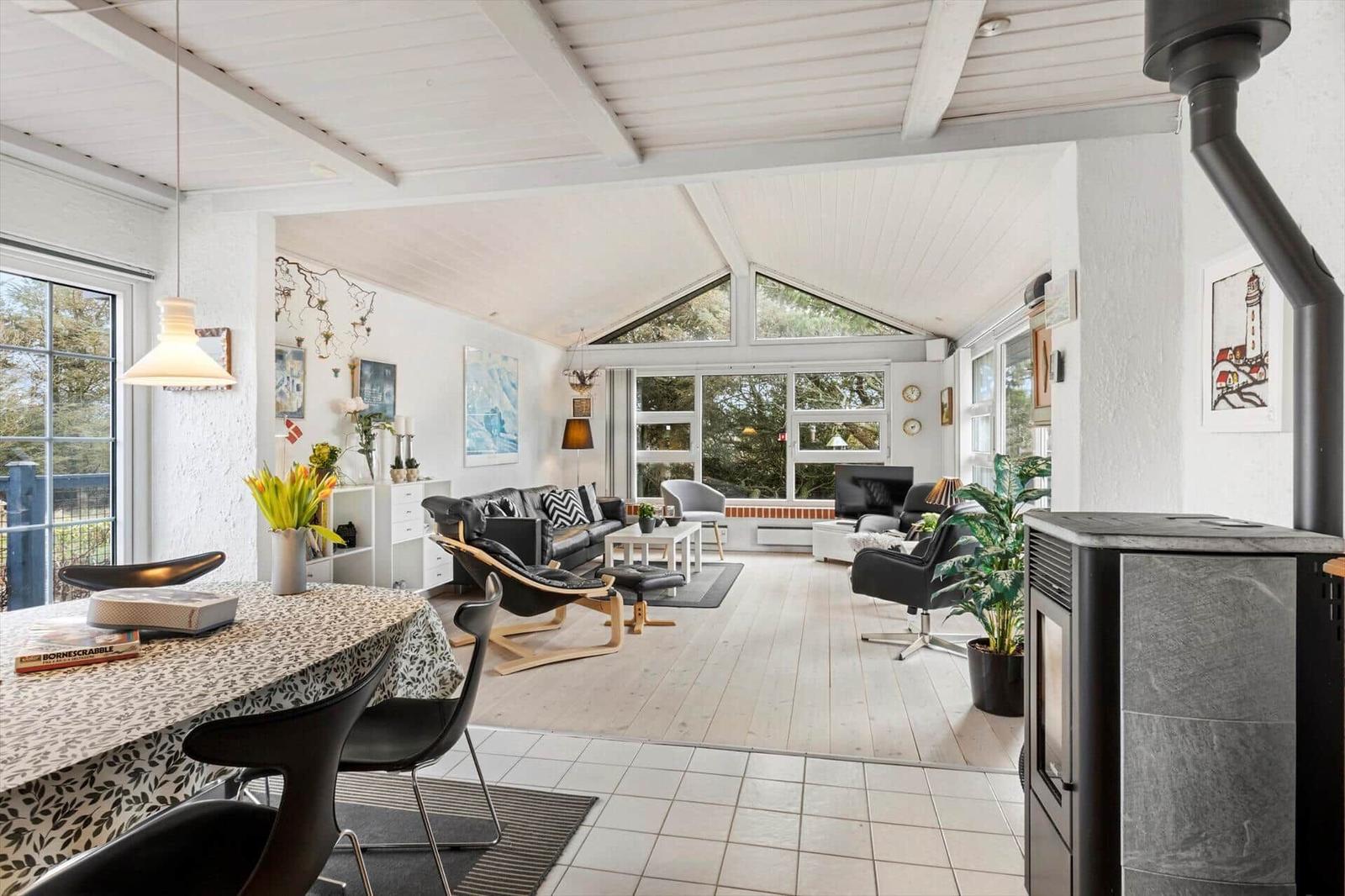 Living and dining area with wooden floor, large windows, and wood stove.