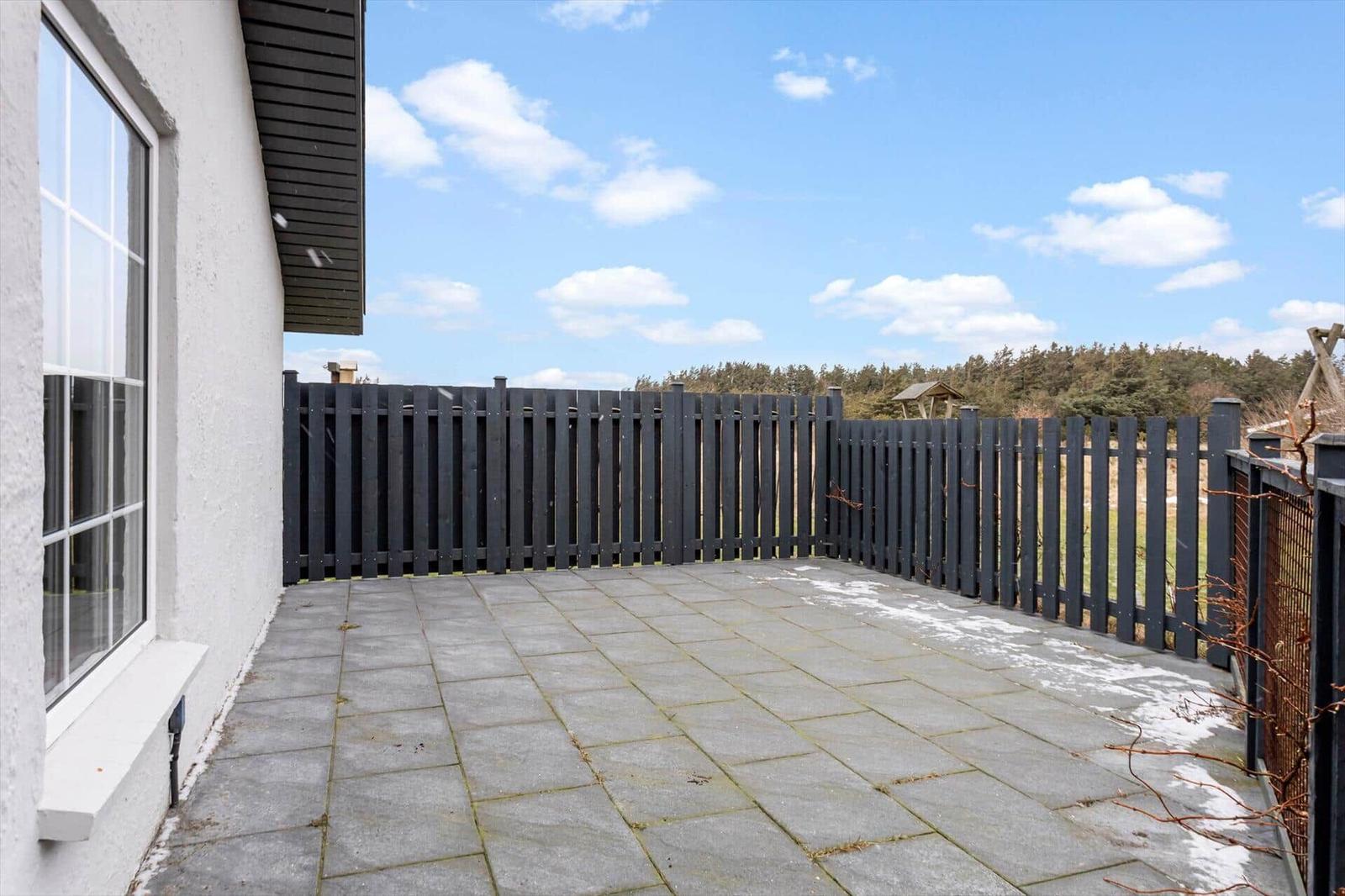 Terrace with stone slabs and black wooden border. Background: forest and blue sky.