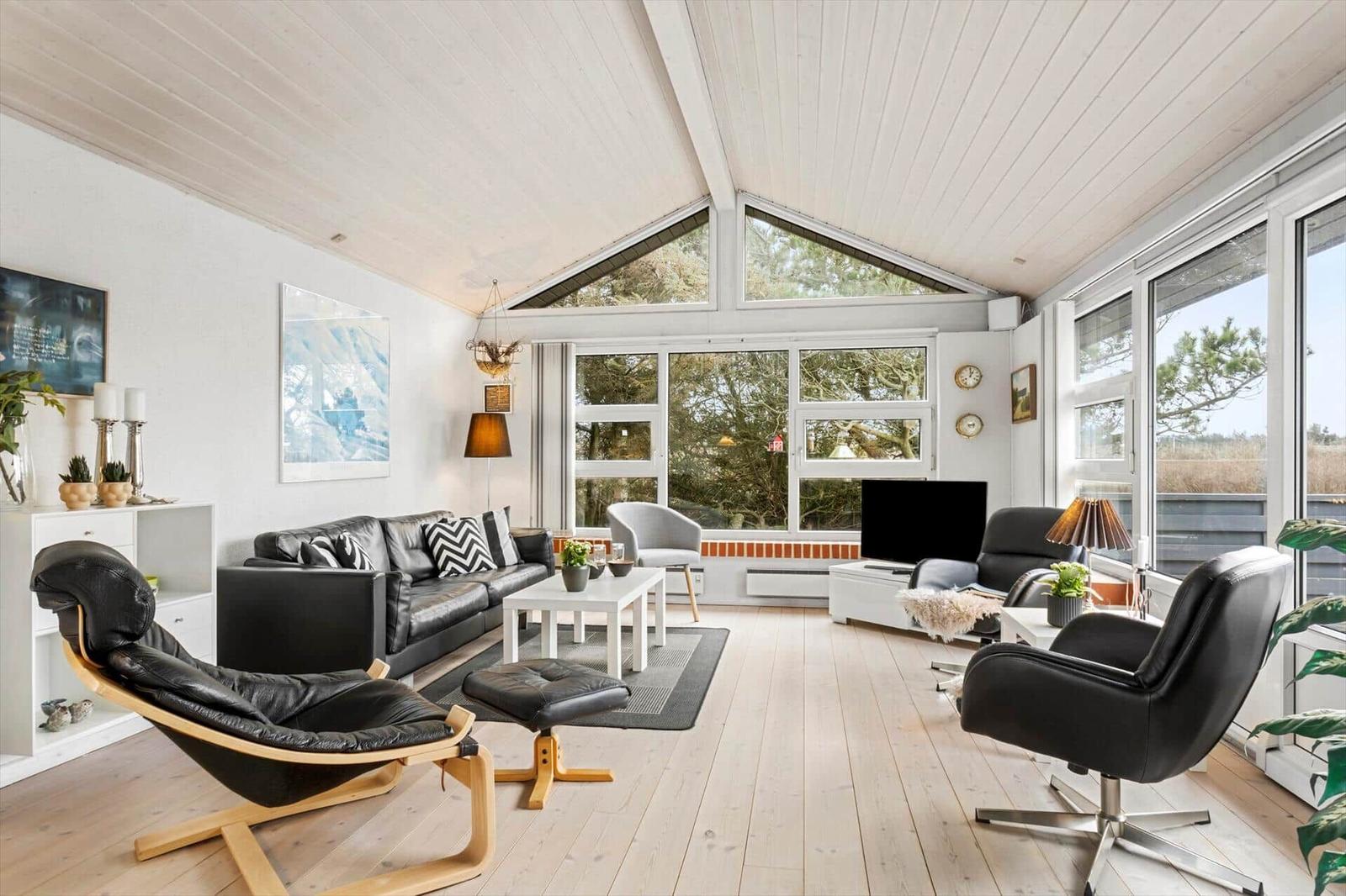 Living room with black leather furniture, wooden floor, and large windows.