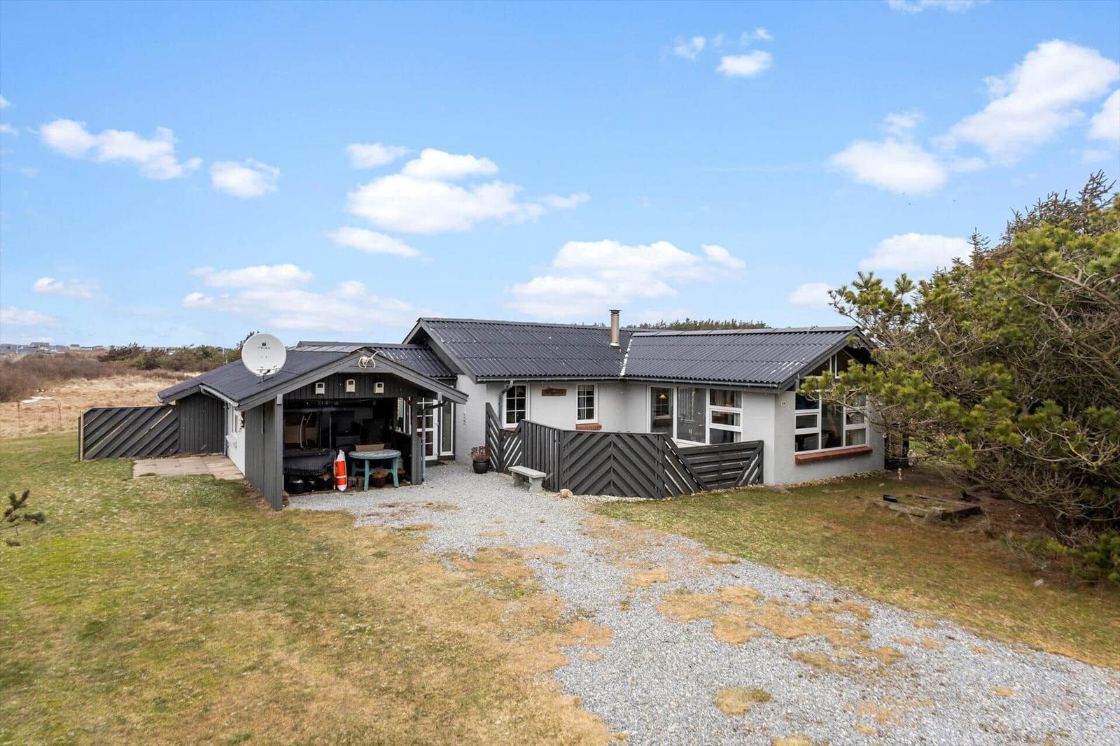 A house with gray roof and white facade. Courtyard with gravel path and wooden railings.