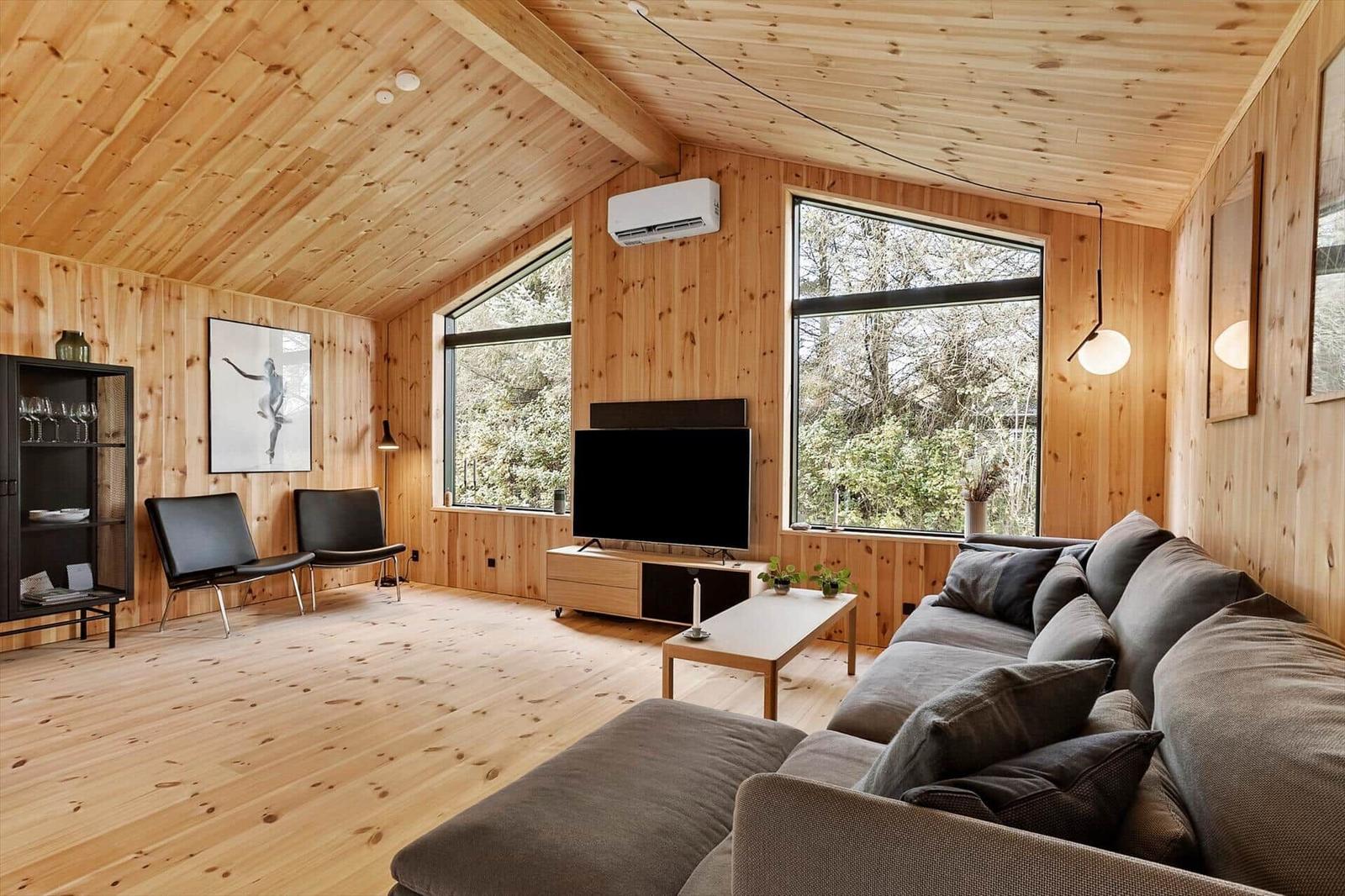 Living room with wooden walls, sofa, TV, and large windows.