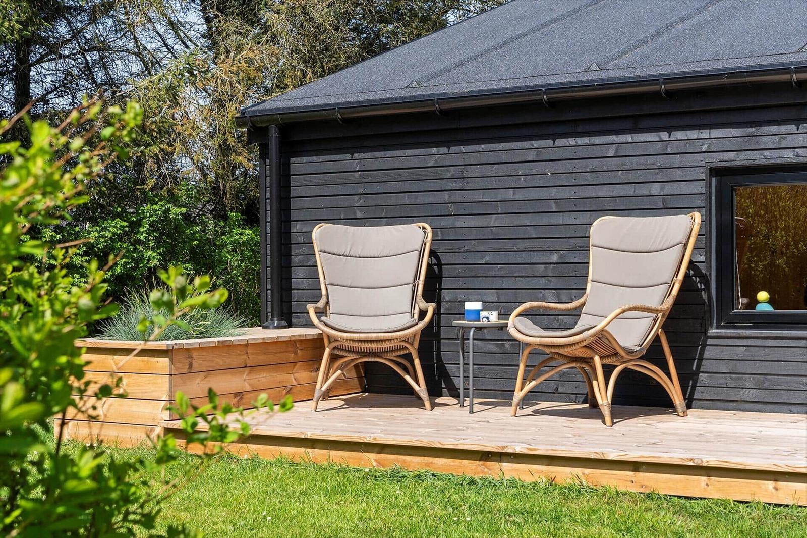 Two rattan chairs with cushions are on a terrace in front of a house.