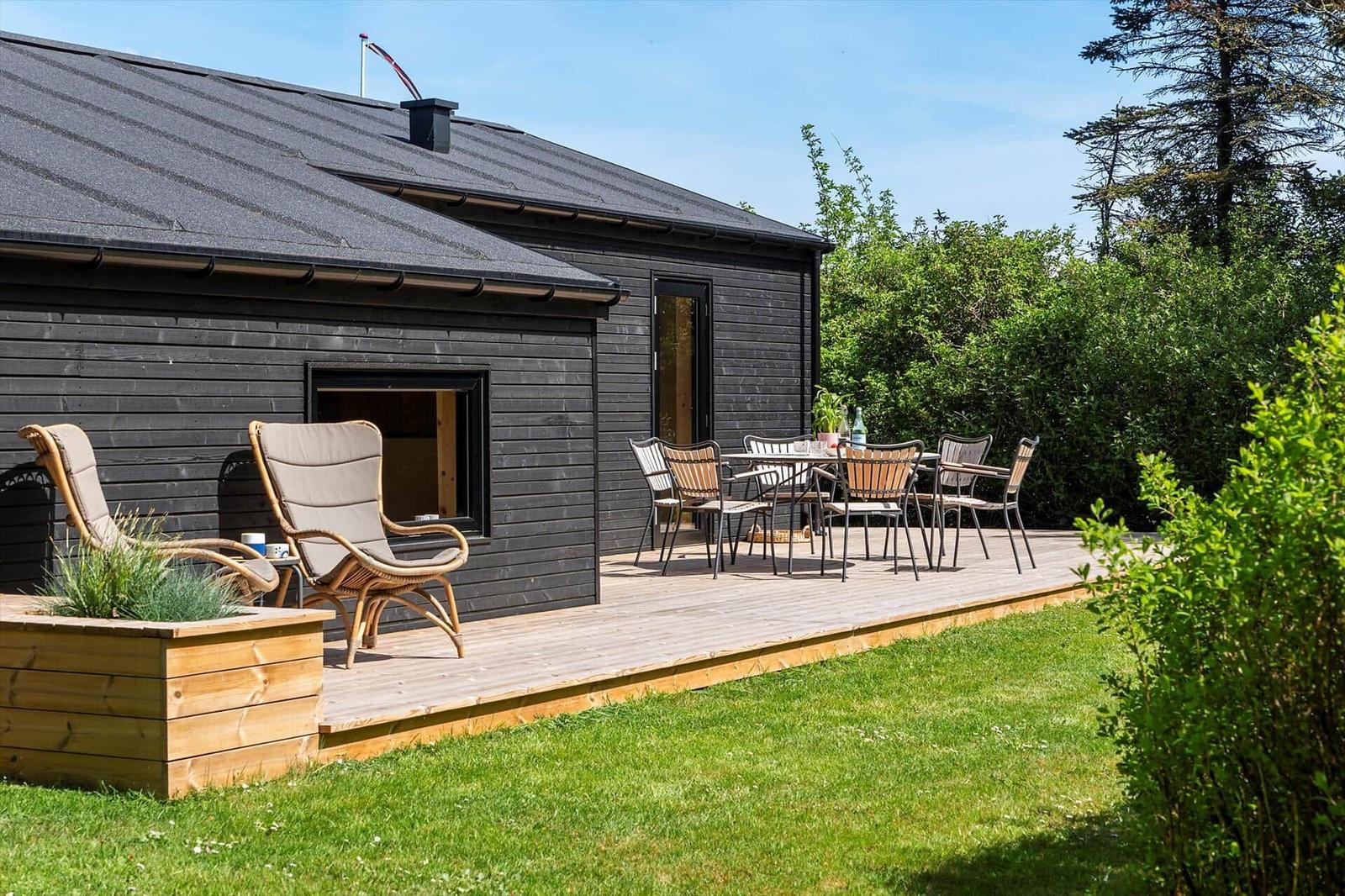 Black wooden house with terrace, garden furniture, and plants.