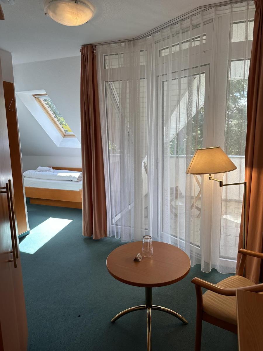 Zimmer mit Blick auf Balkon, Tisch, Stuhl und Bett im Hintergrund.
