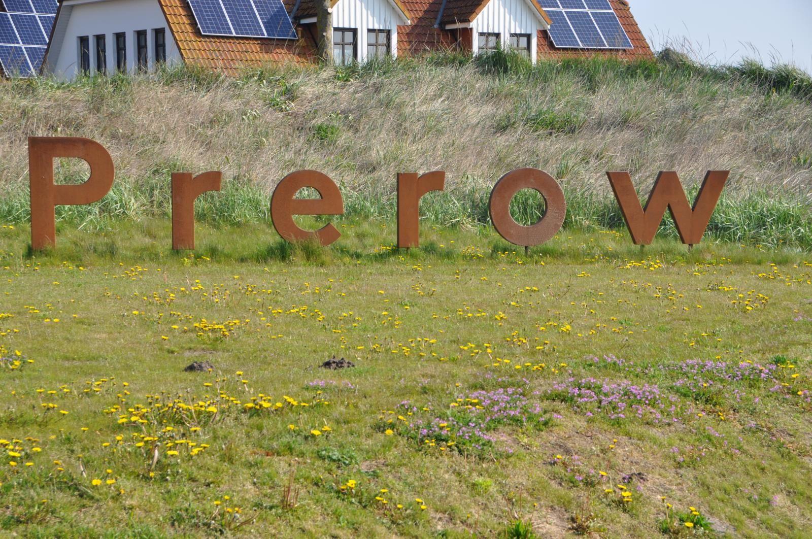 Large sign with the name Prerow on a green meadow with blooming flowers.
