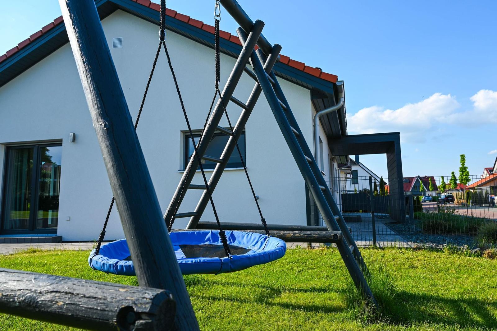 Ein blauer Klettergerüst mit Schaukel steht im Garten vor einem Haus.