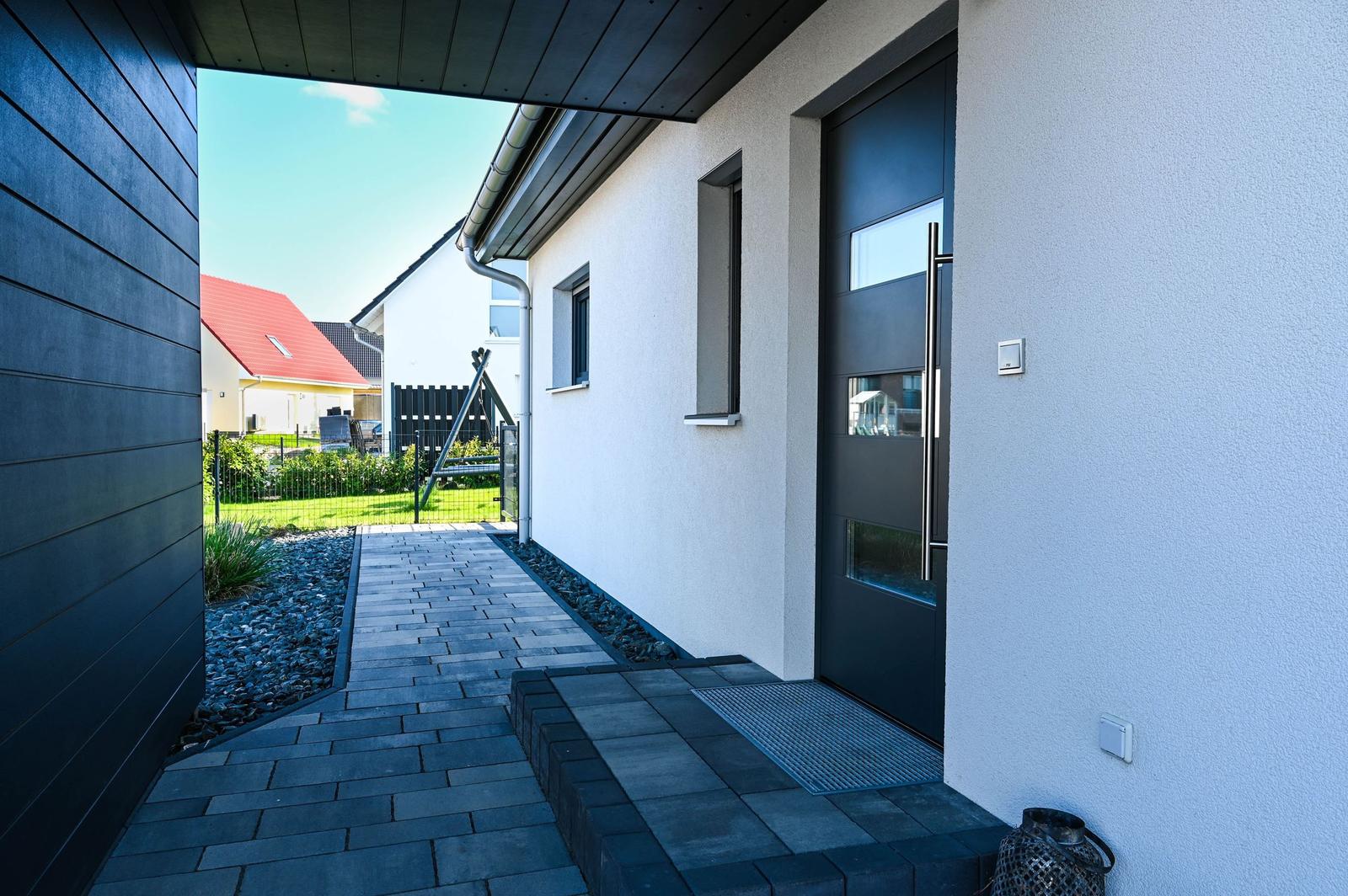 Moderne Eingangstreppe mit schwarzem Holz und grauem Kiesweg führt zur Haustür.