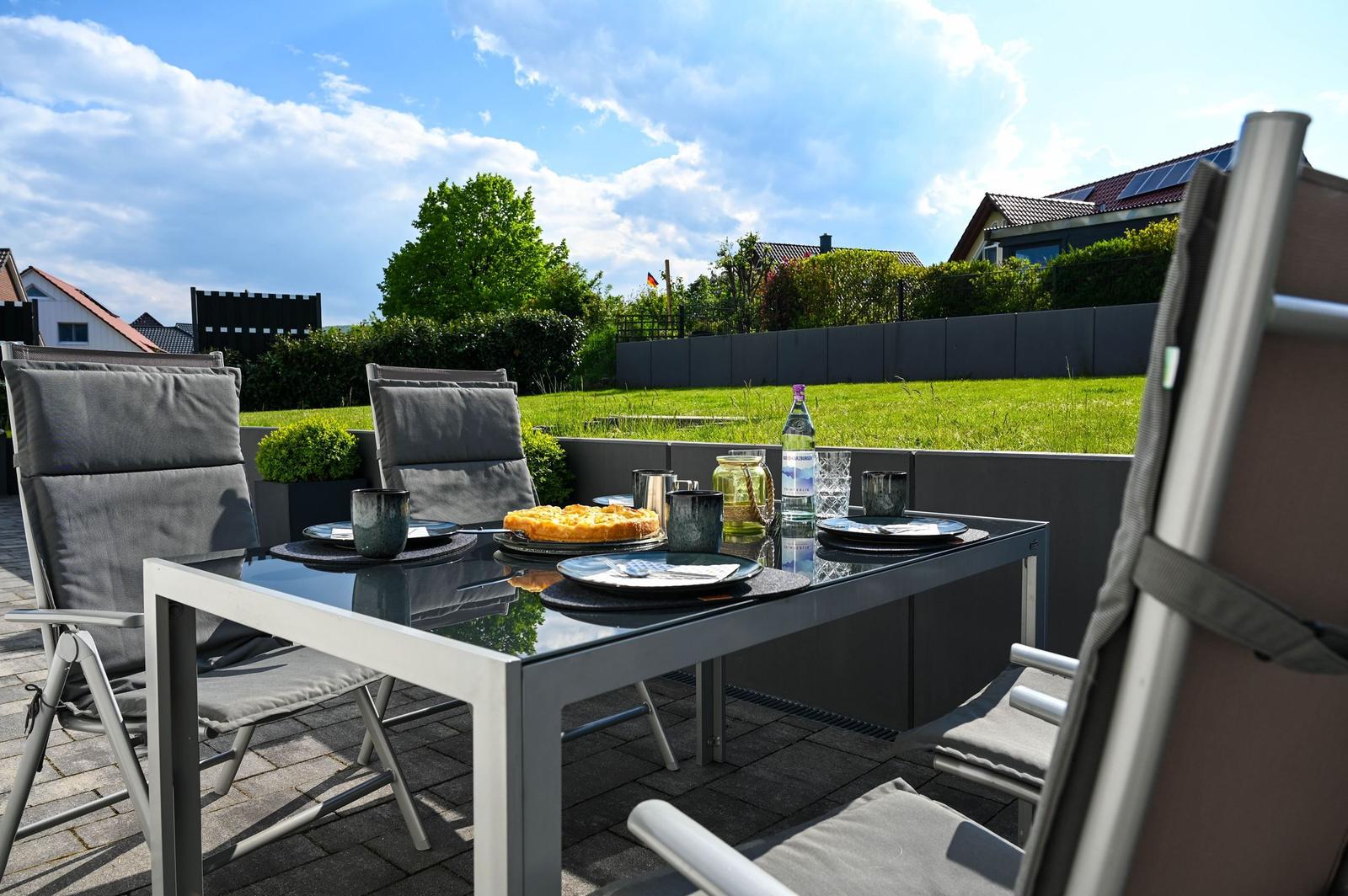 Terrasse mit Gartentisch, Stühlen und Essen im Freien.