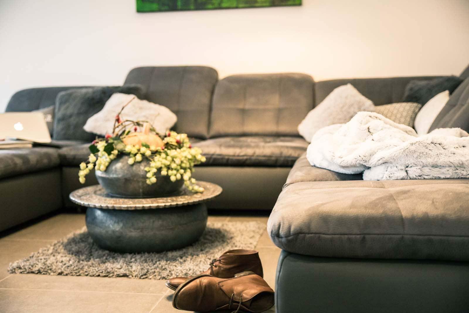 Ein grauer Sofa-Bereich mit Kissen, Decke und einem runden Tisch mit Blumen.