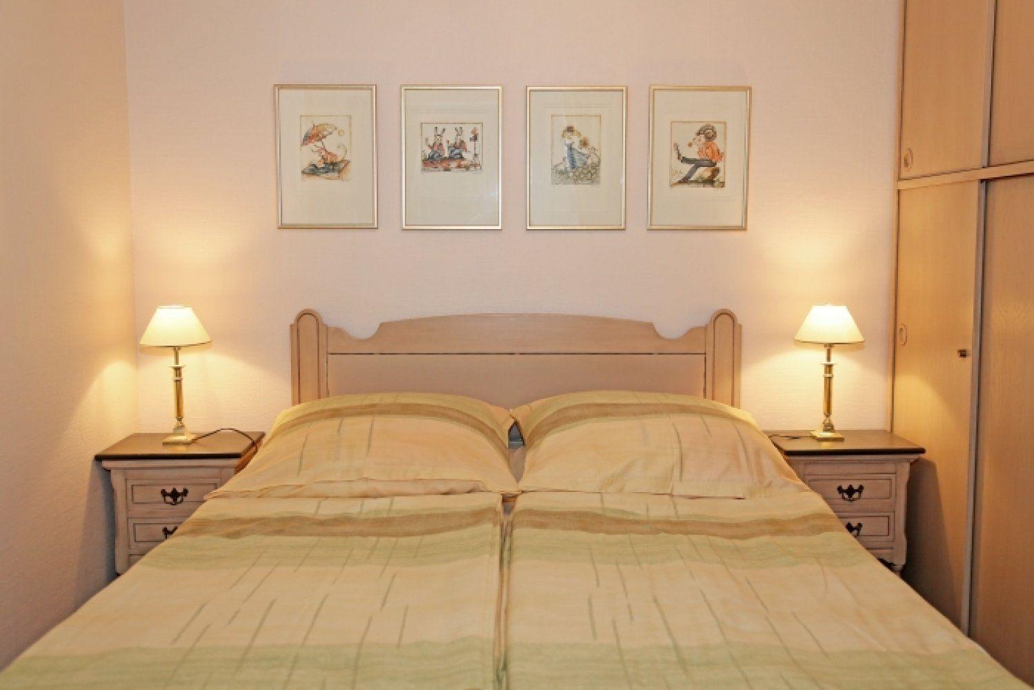 Doppelbett mit zwei Nachttischen und Lampen. An der Wand hängen vier gerahmte Bilder.