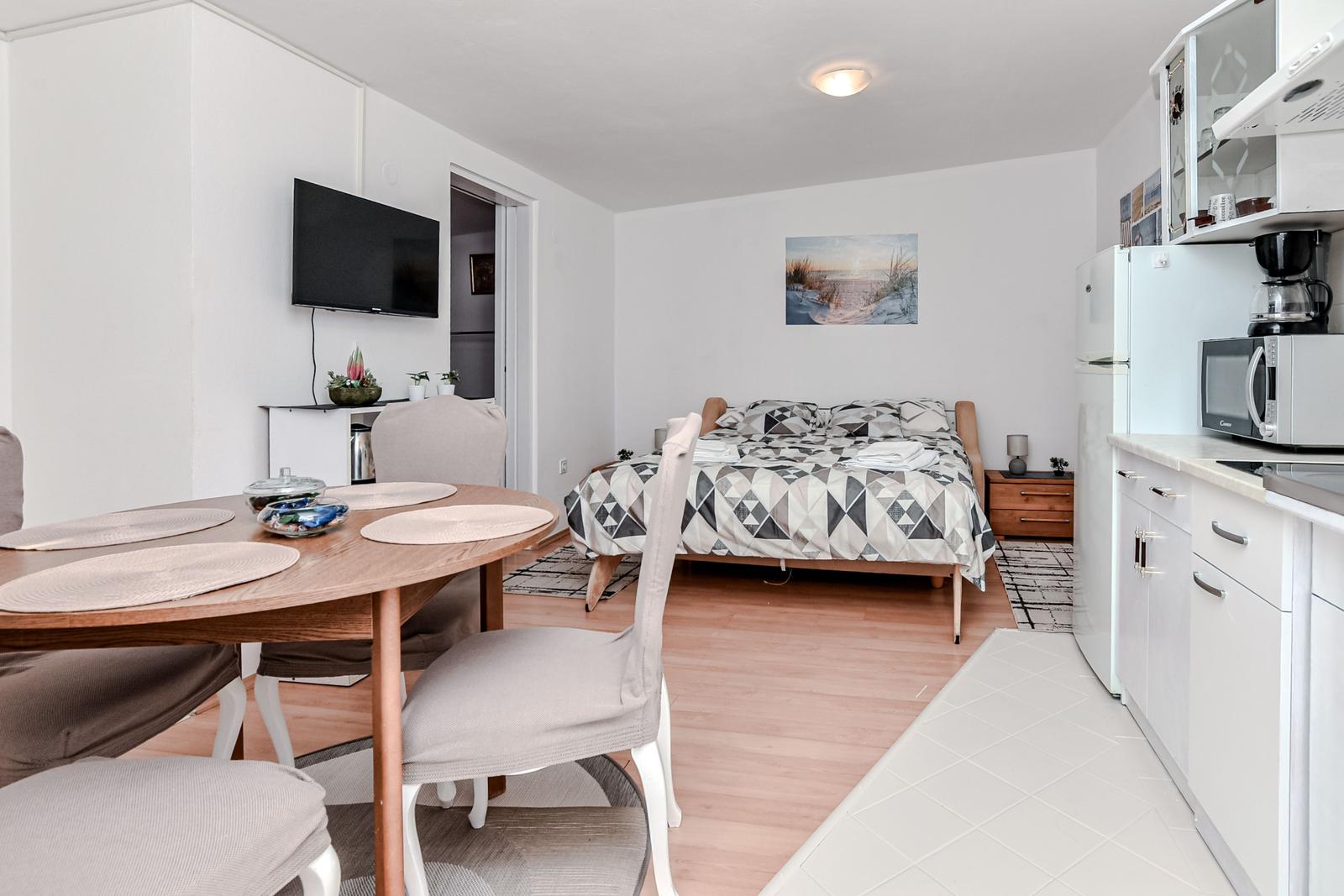 Schlafzimmer mit Bett, Wohnbereich mit Tisch und Küche mit Küchenschränken.