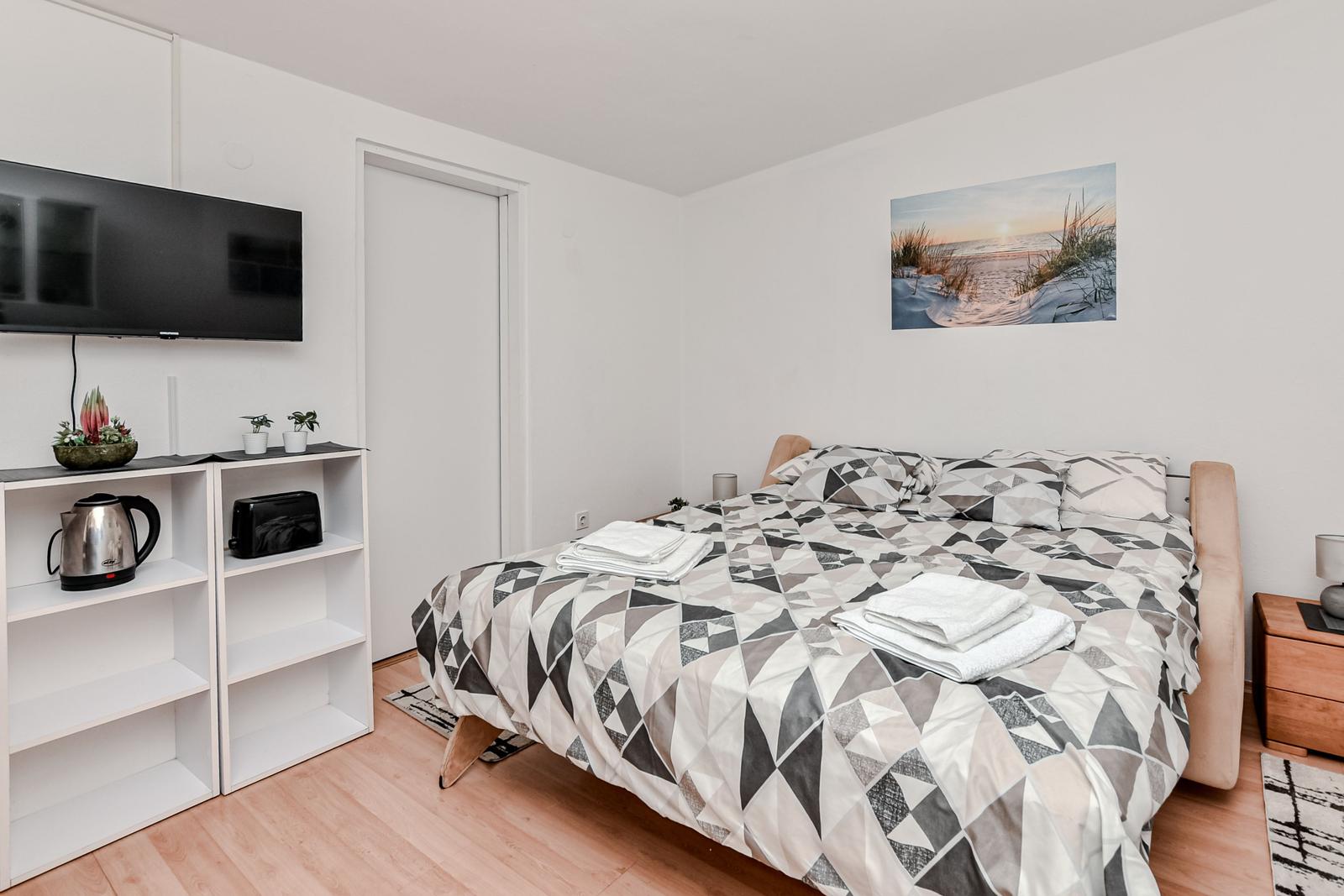 Schlafzimmer mit Bett, Fernseher und Küchenutensilien.