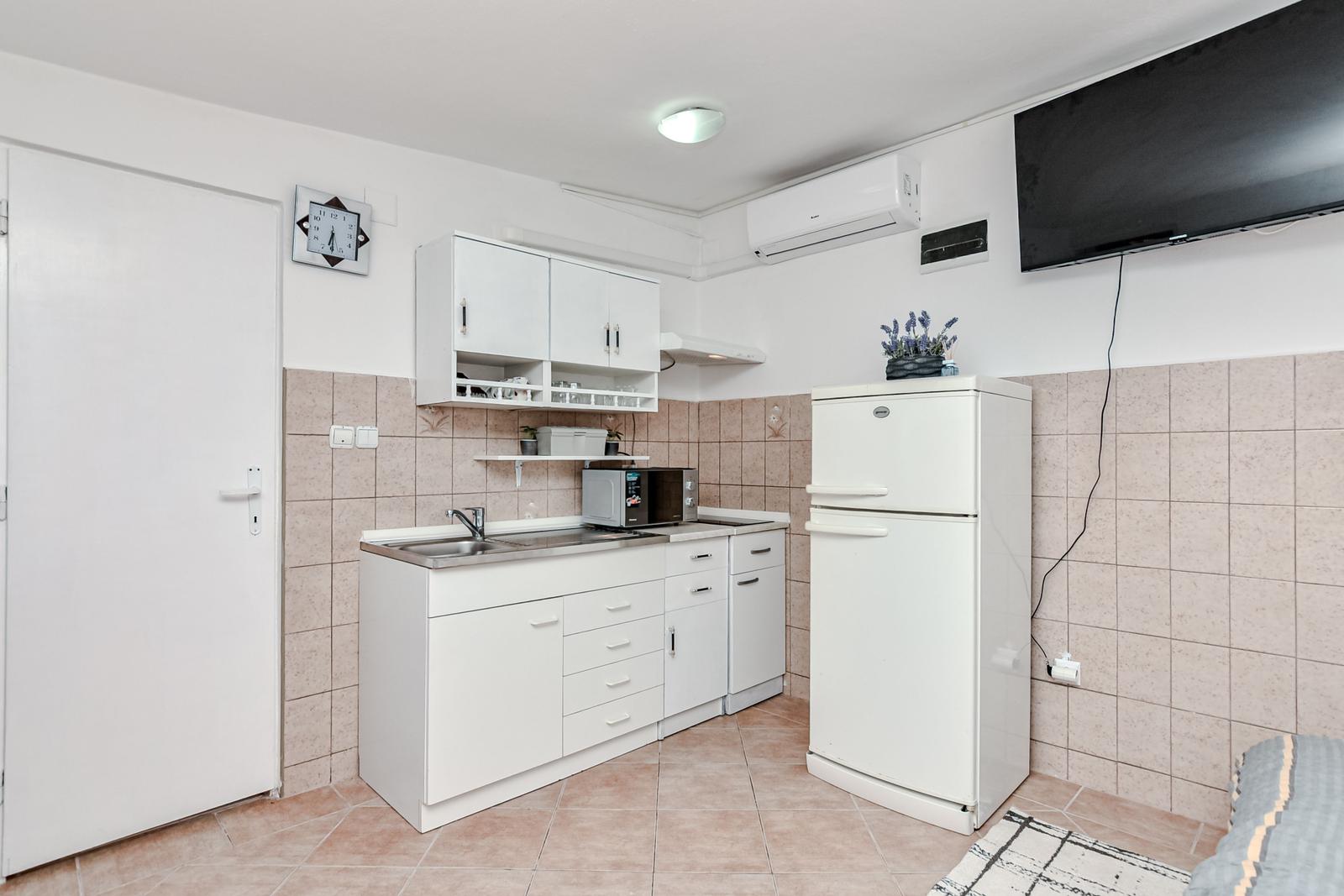 Küche mit weißen Schränken, Kühlschrank und TV an der Wand.