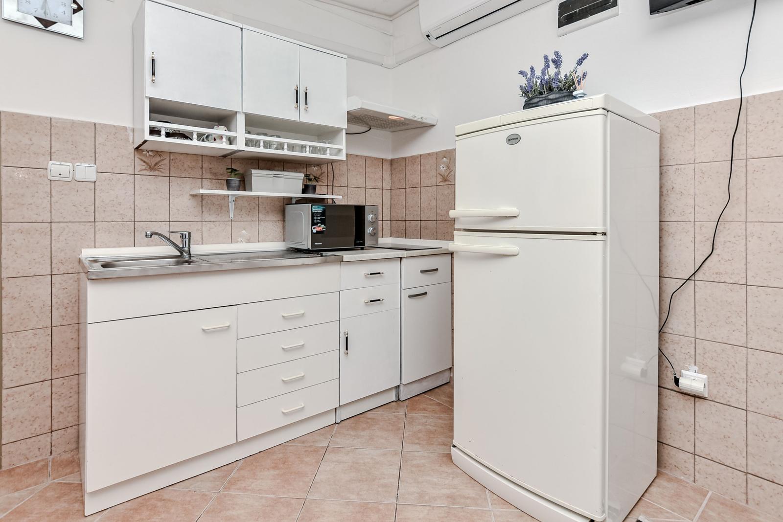 Küche mit weißen Schränken, Kühlschrank und Mikrowelle.