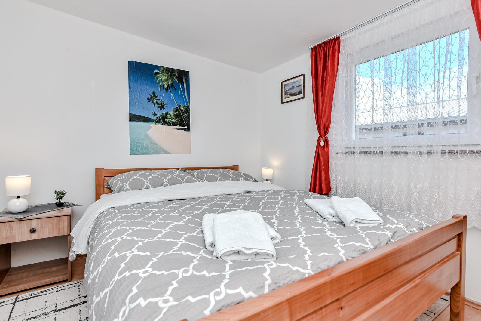 Schlafzimmer mit Bett, Nachttisch und Fenster mit roten Vorhängen.