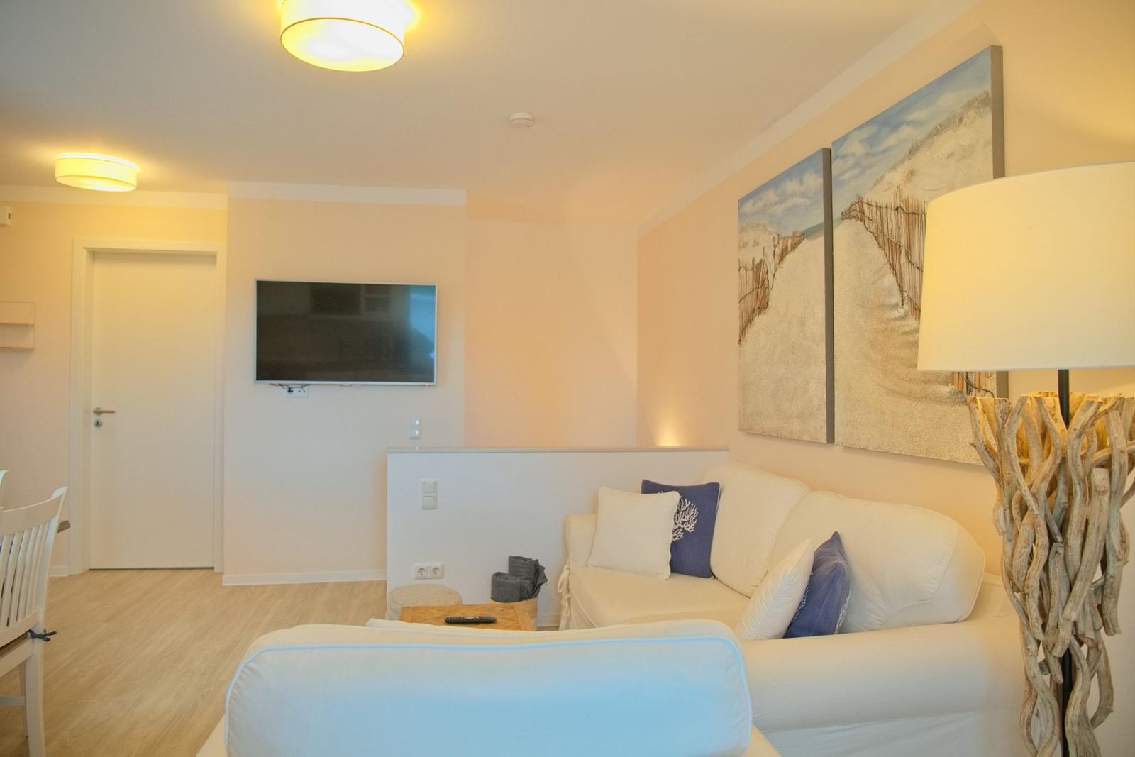 Wohnzimmer mit Sofa, Fernseher und Strandmotiv an der Wand.