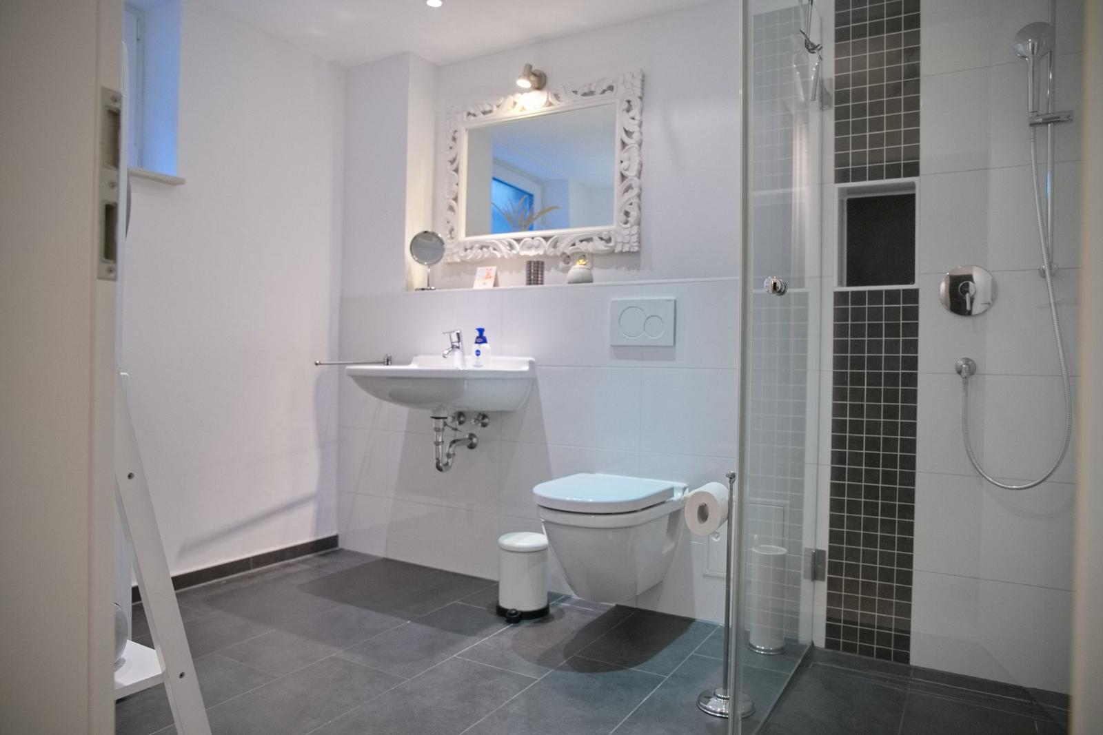 Badezimmer mit Dusche, Waschbecken und Toilette. Fliesen und Spiegel sind sichtbar.