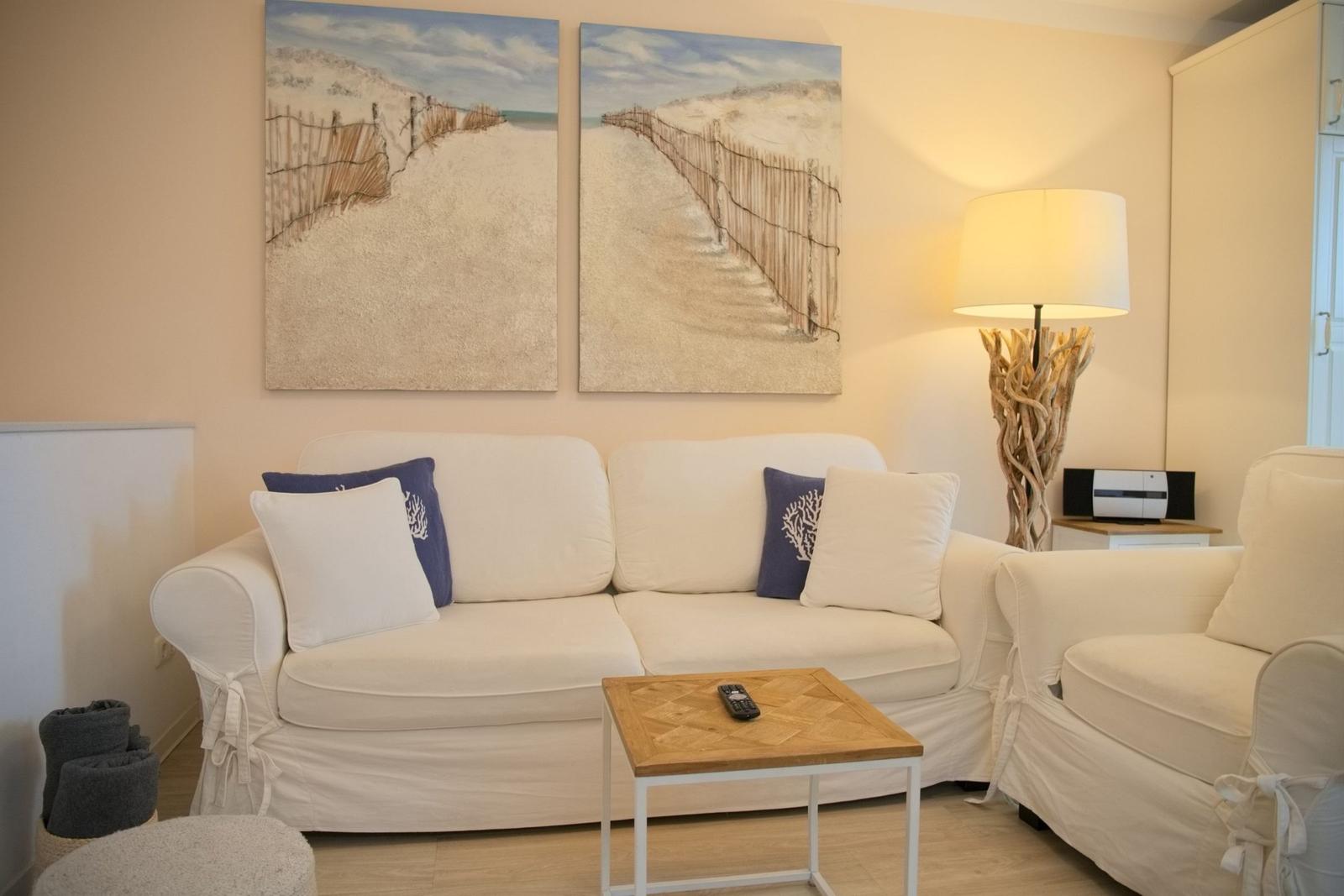 Wohnzimmer mit Sofa, Sessel und Tisch. Wandbild zeigt Strand. Stehlampe mit Holzgestell.
