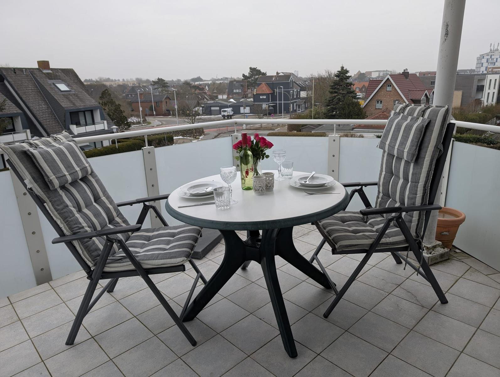 Terrasse mit Tisch und zwei Stühlen, gedeckt für zwei Personen mit Blumen und Gläsern.