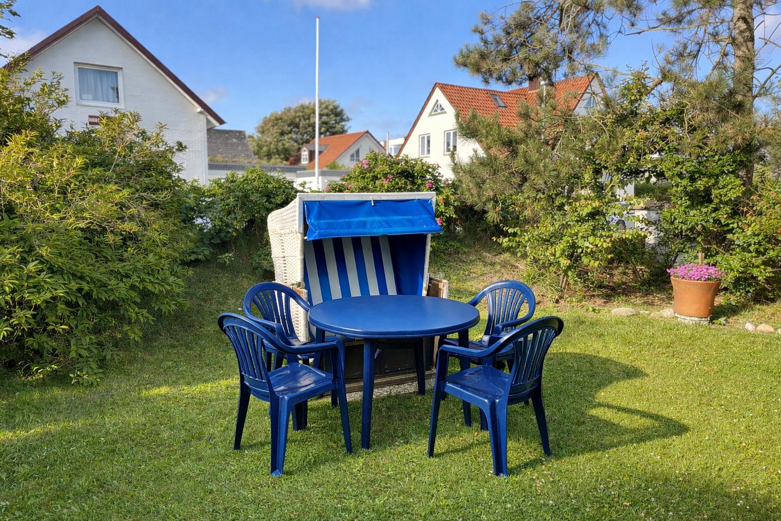 Garten mit blauem Tisch, vier Stühlen und Strandkorb.