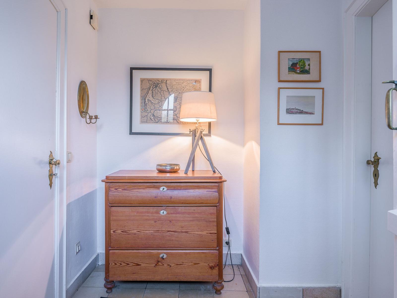 Hallen mit Holzschrank, Lampe und Bildern an den Wänden.