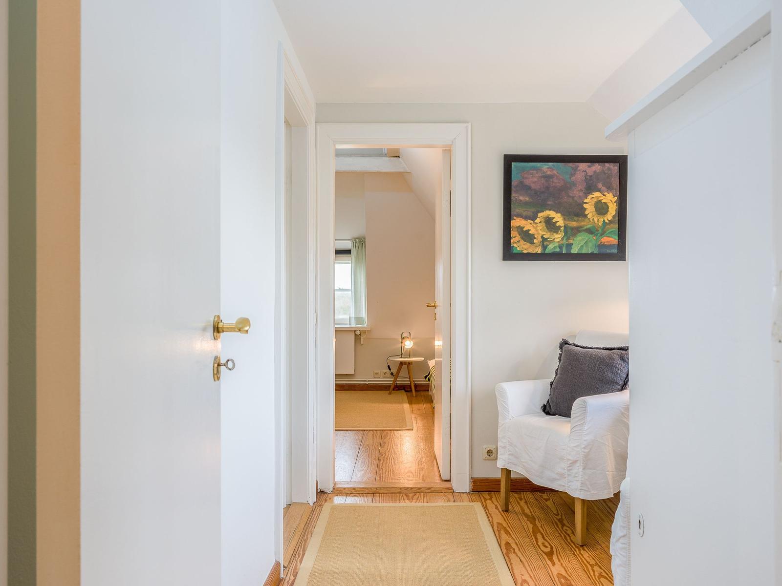 Flur mit Sitzgelegenheit und Bild an der Wand. Durchgang zu einem Zimmer mit Holzboden.