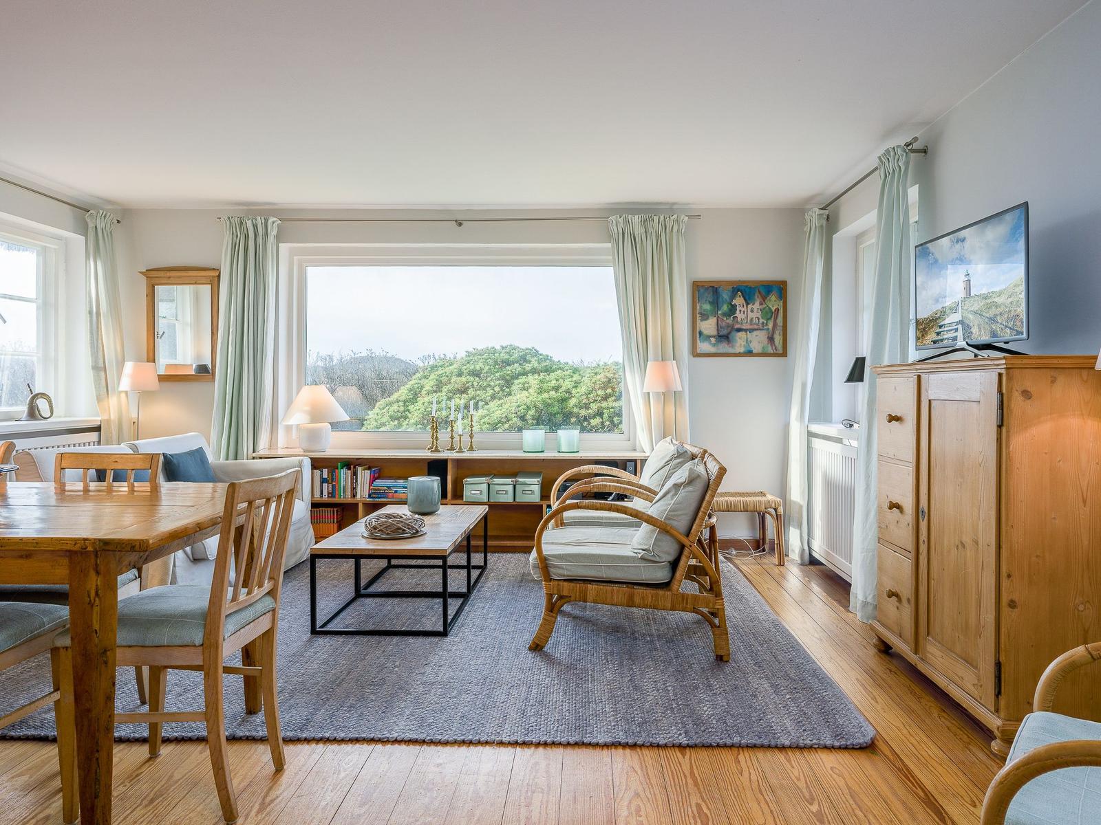 Wohn- und Essbereich mit Holzmöbeln und Blick auf Grünflächen.