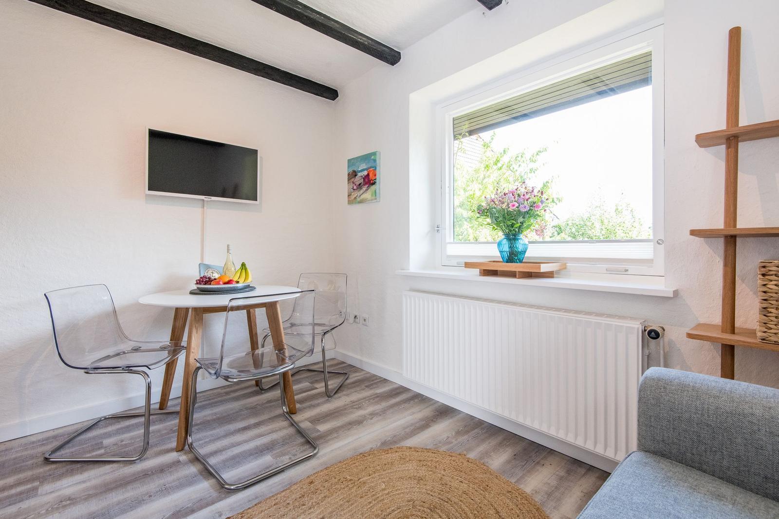 Raum mit Esstisch, TV und Fenster mit Blumen.