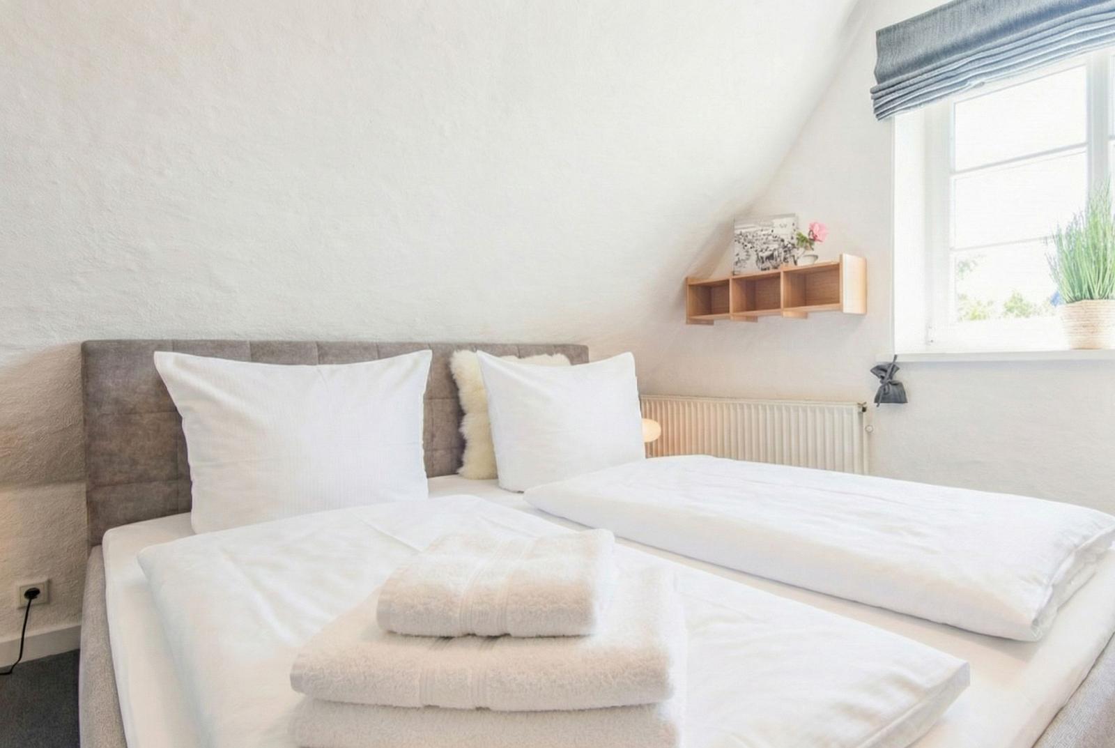 Schlafzimmer mit Doppelbett, weißen Laken und Fenster mit Pflanze.