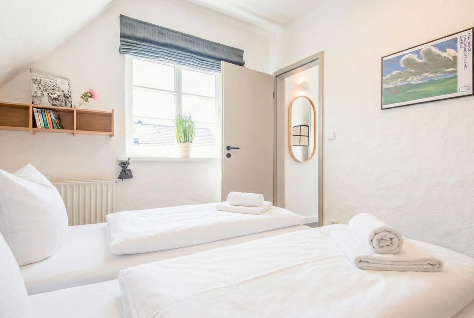 Zwei Betten mit weißen Bettwäschen, Fenster mit grünem Vorhang und Wandbild.