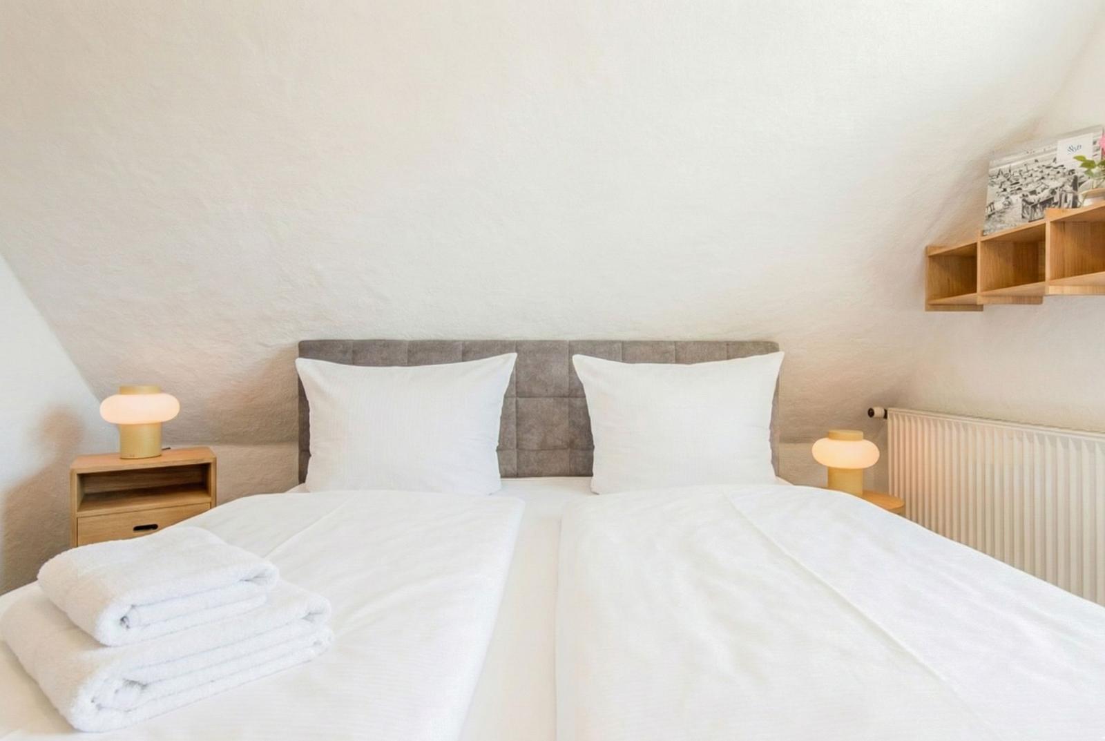 Schlafzimmer mit Doppelbett, Nachttischen und Holzregal an der Wand.