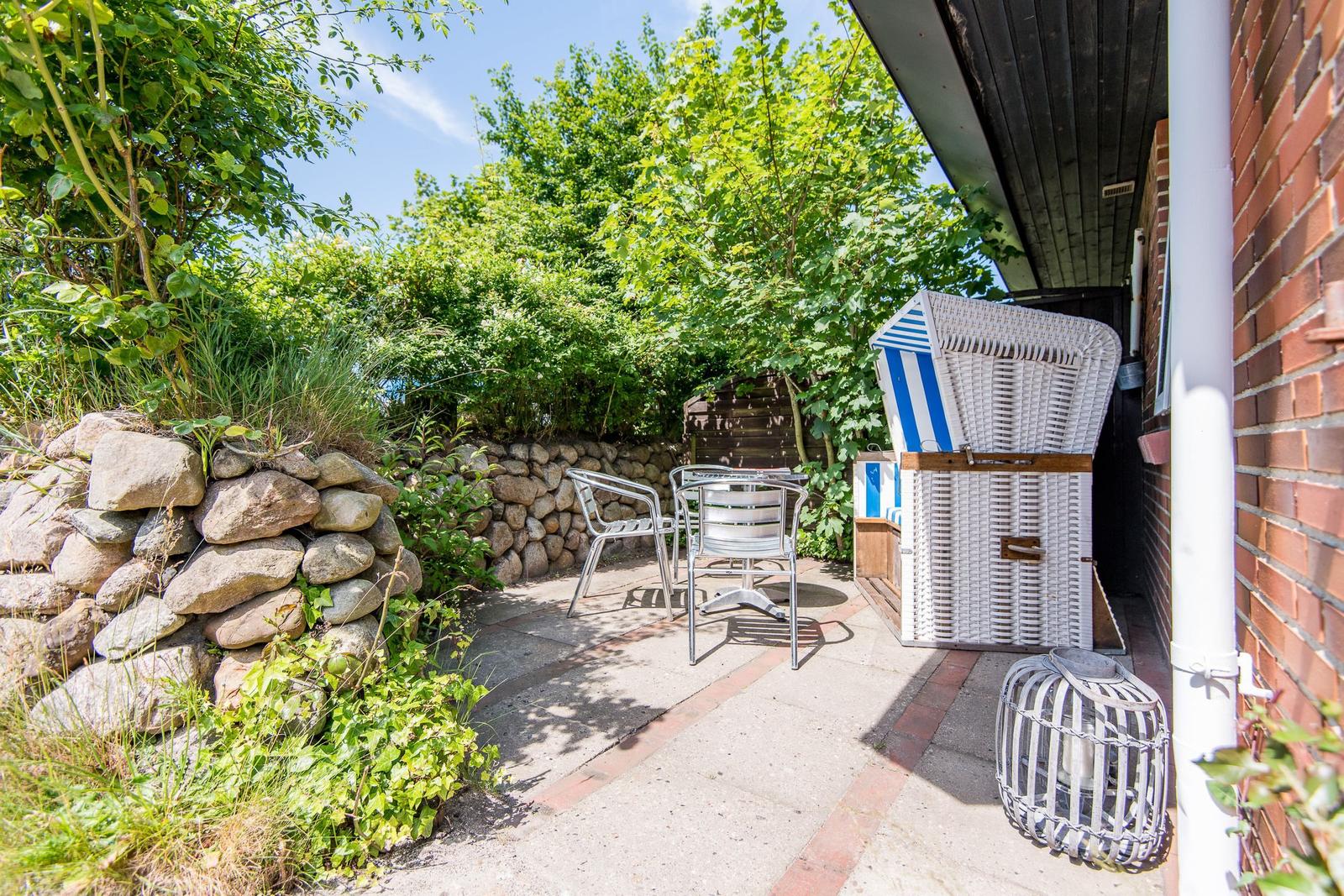 Terrasse mit Stuhl, Tisch und Strandkorb neben Steinmauer und Backsteinhaus.