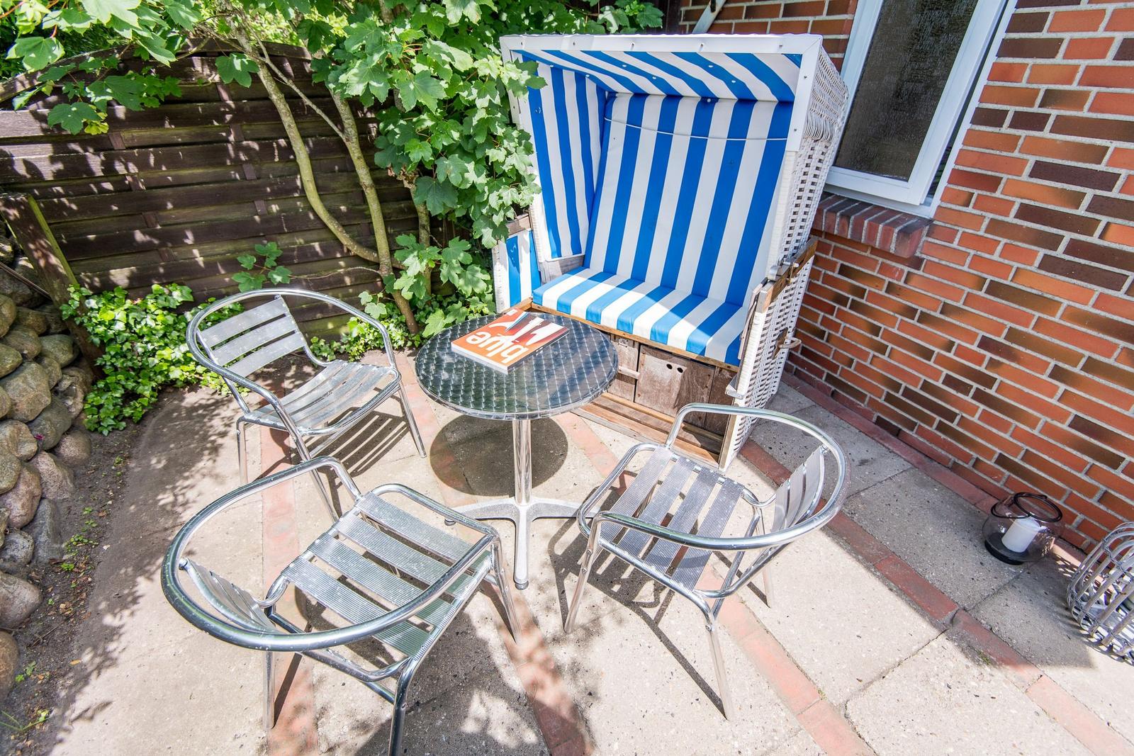 Terrasse mit Strandkorb, Tisch und drei Stühlen neben Backsteinmauer