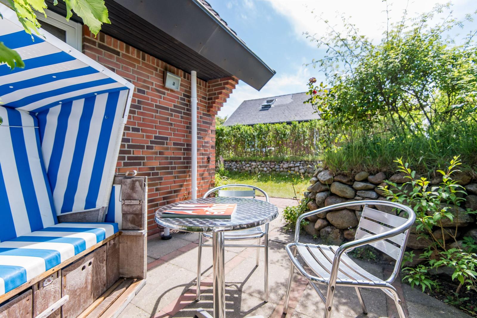Terrasse mit Strandkorb, Tisch und Stühlen neben Backsteinhaus.