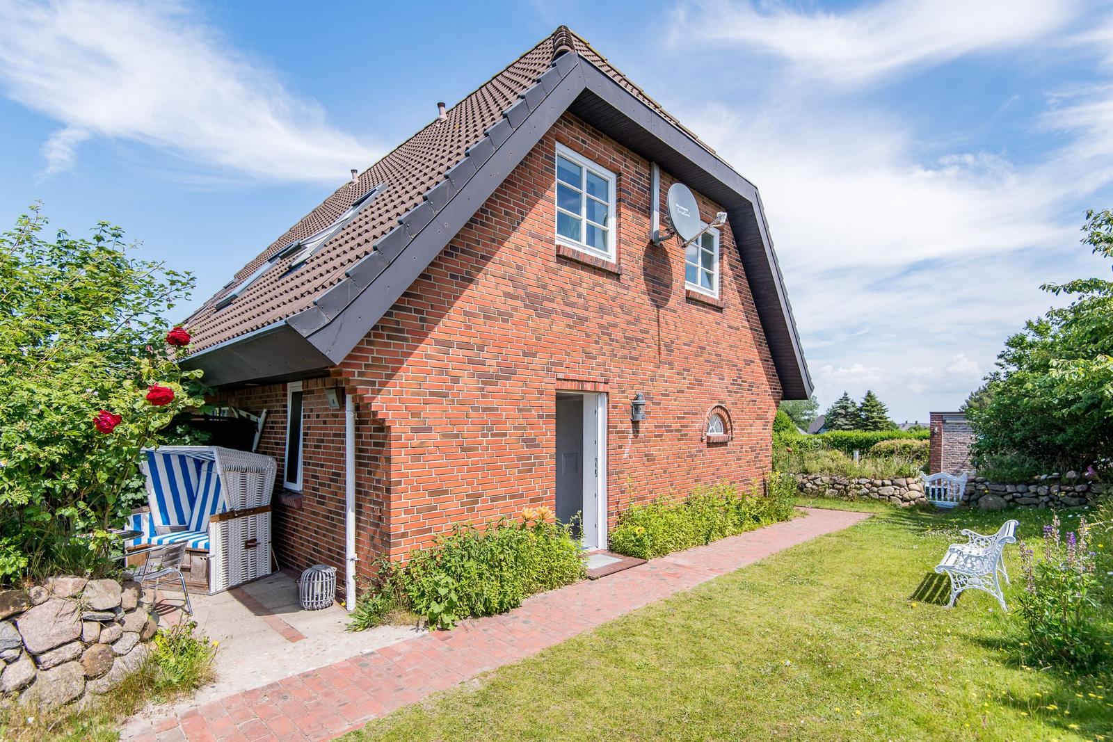 Rotes Backsteingebäude mit Garten, Terrasse und weißen Gartenmöbeln.